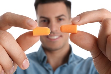 Photo of Man with foam ear plugs against white background, focus on hands