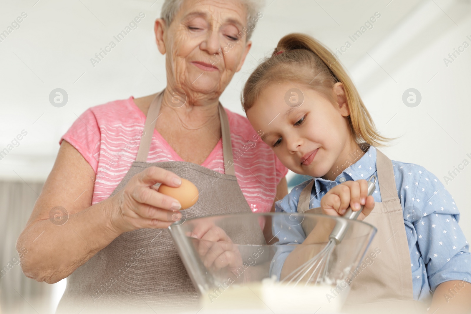 Photo of Cute girl and her grandmother cooking in kitchen