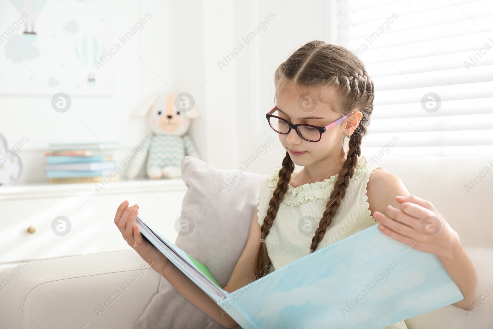 Photo of Cute little girl reading book on sofa at home
