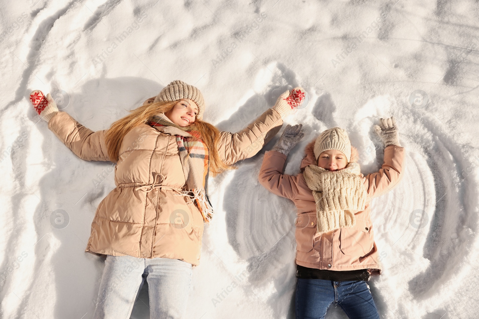 Photo of Family time. Happy mother and her daughter making snow angels on sunny winter day, above view