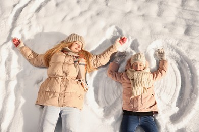 Family time. Happy mother and her daughter making snow angels on sunny winter day, above view