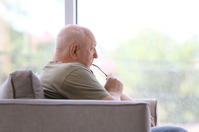 Photo of Depressed senior man sitting in armchair indoors