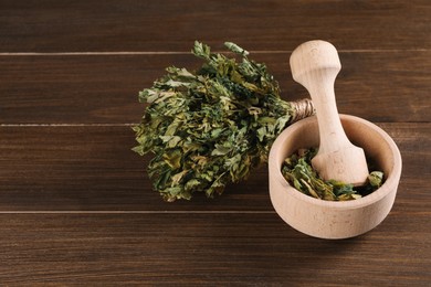 Mortar and pestle with dry parsley on wooden table, space for text