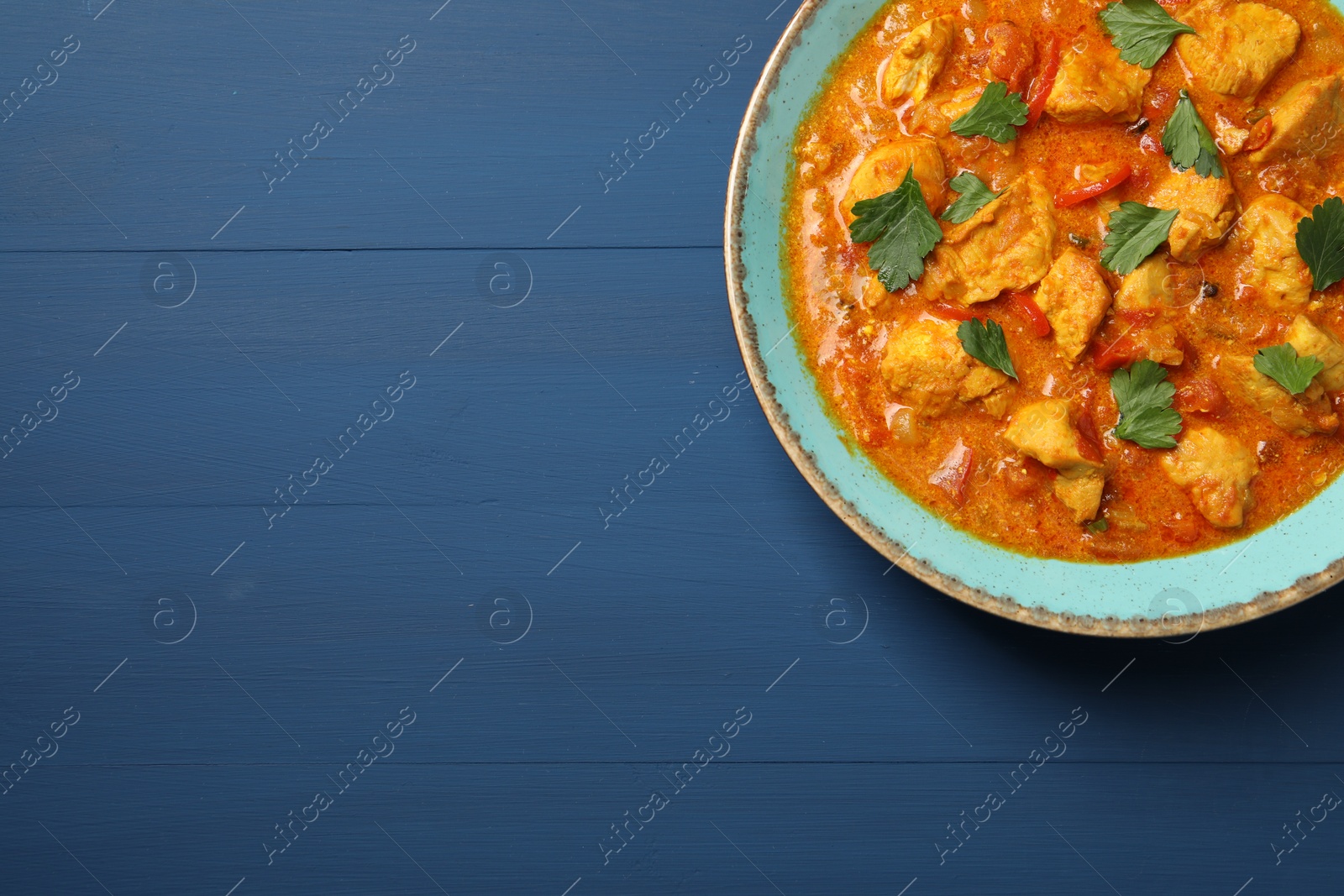 Photo of Delicious chicken curry on blue wooden table, top view. Space for text