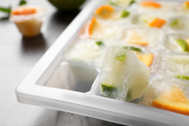 Photo of Ice cube tray with frozen fruits on table, closeup