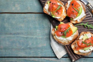 Photo of Delicious sandwiches with cream cheese, salmon, avocado and arugula served on light blue wooden table, flat lay. Space for text