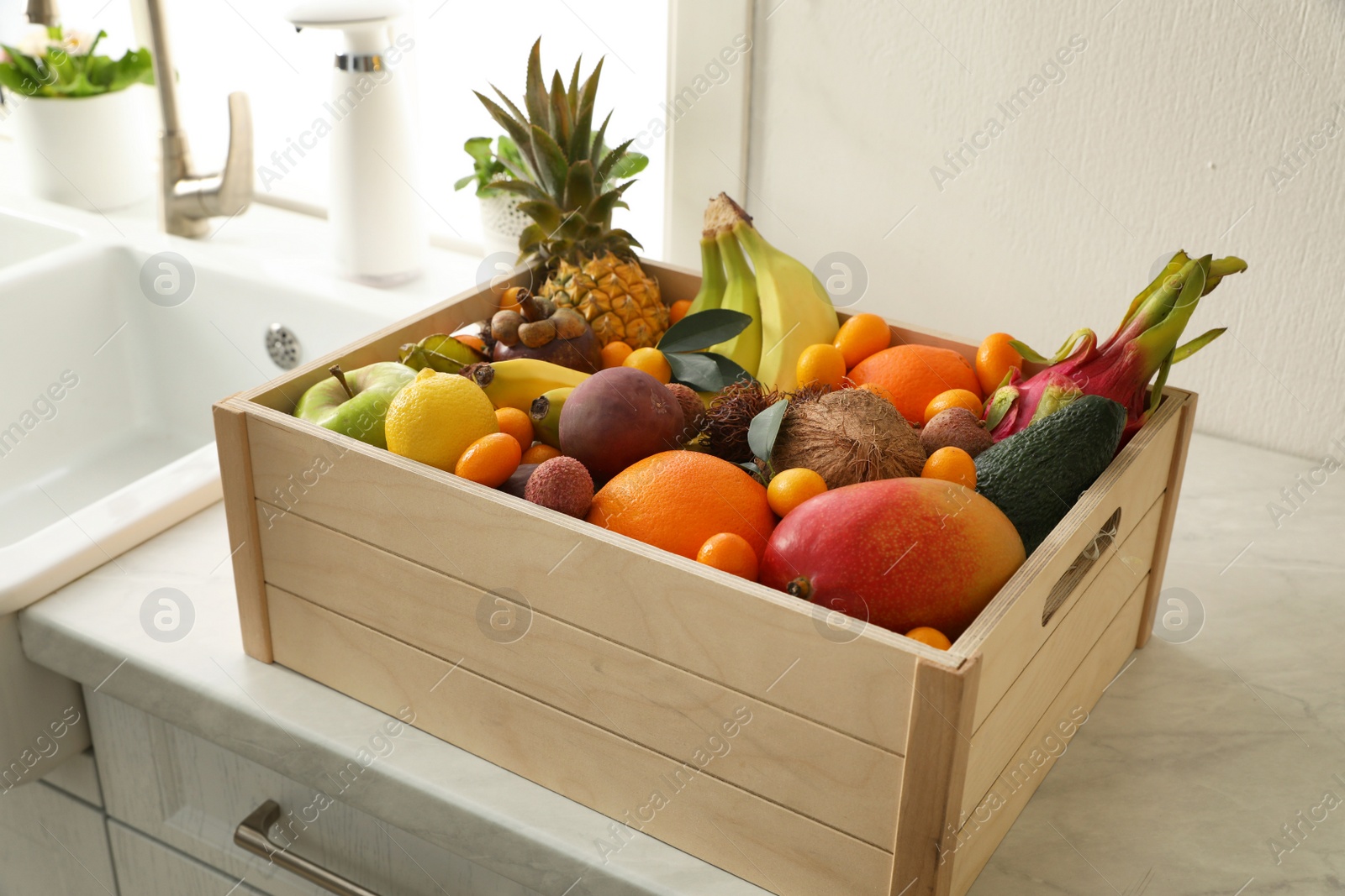 Photo of Wooden crate with assortment of exotic fruits on table in kitchen