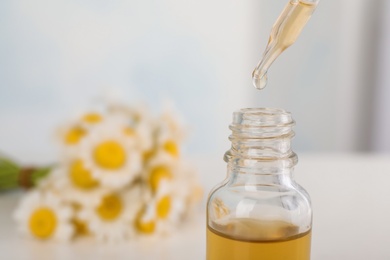 Pipette with essential oil over bottle on blurred background, closeup. Space for text