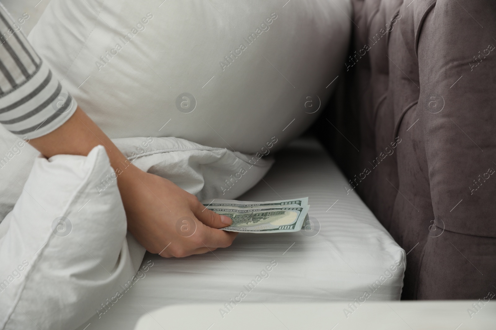 Photo of Woman hiding dollar banknotes under pillow in bedroom, closeup. Money savings