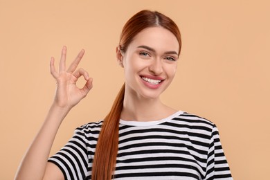 Photo of Beautiful woman with clean teeth showing ok gesture on beige background
