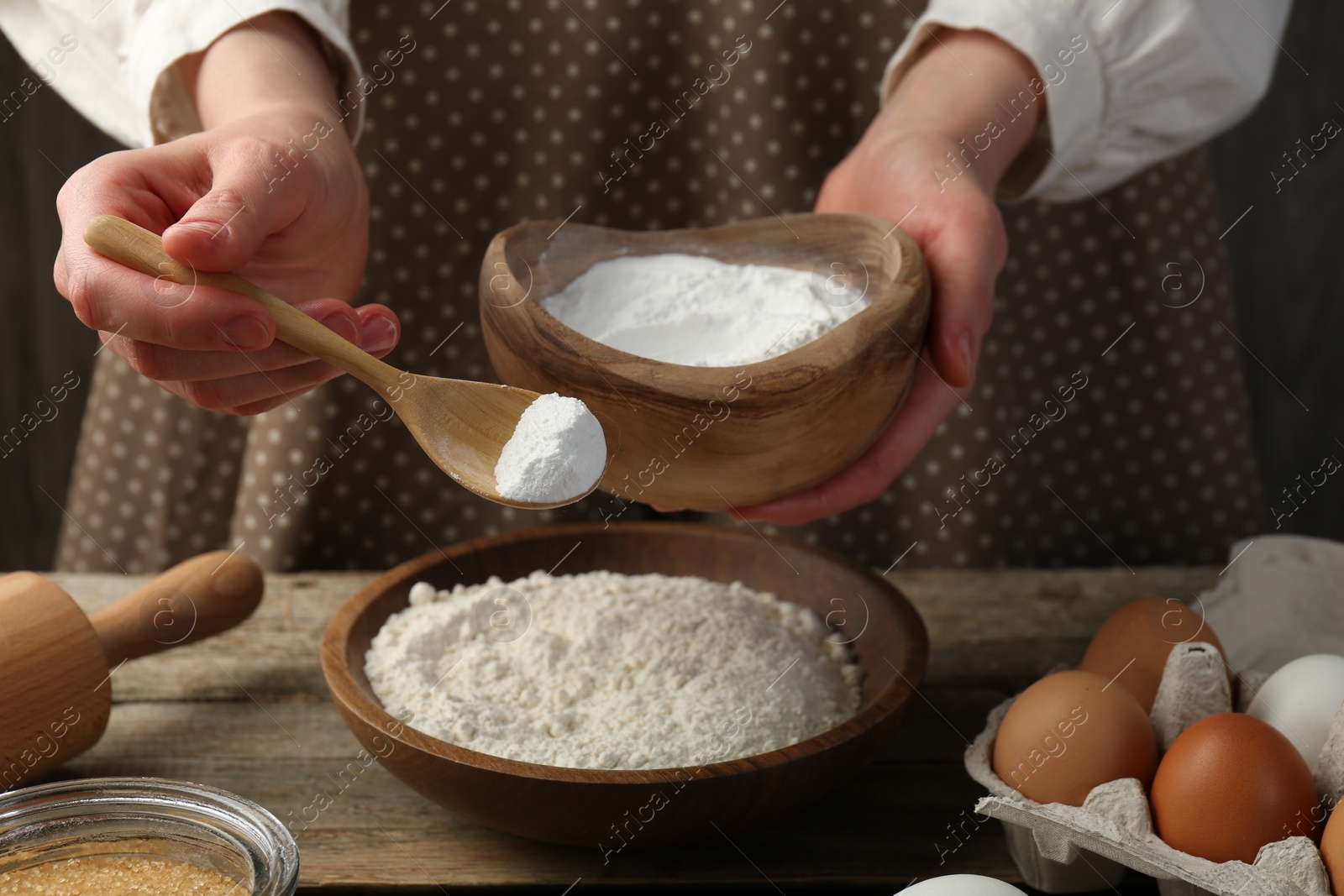 Photo of Making dough. Woman adding baking powder to flour at wooden table, closeup