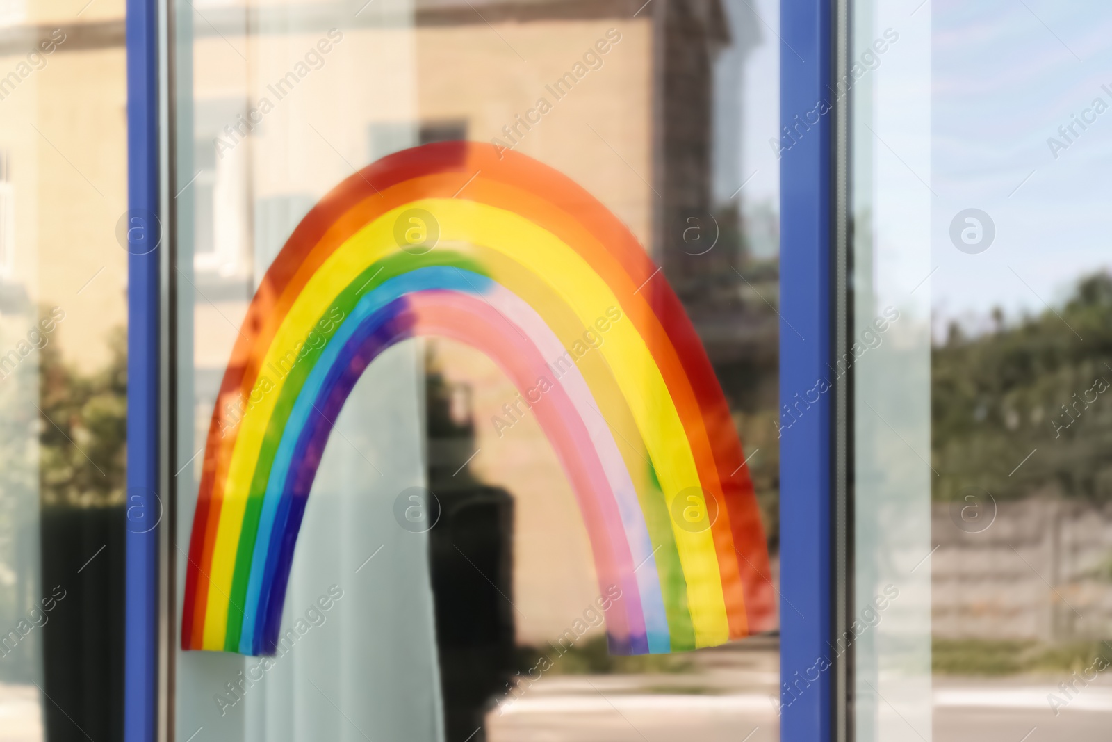 Photo of Painting of rainbow on window, view from outdoors. Stay at home concept