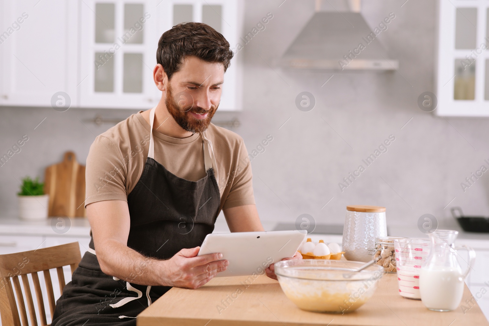 Photo of Man making dough while watching online cooking course via tablet in kitchen