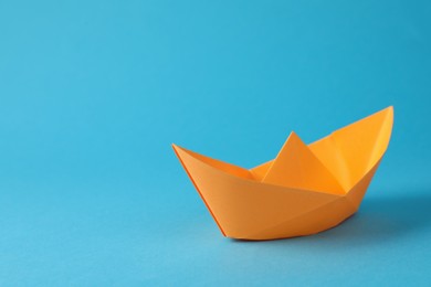 Handmade orange paper boat on light blue background. Space for text