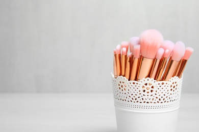 Photo of Organizer with professional makeup brushes against light background. Space for text