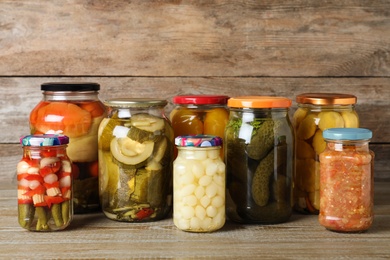Photo of Jars with pickled vegetables on wooden table against brown background