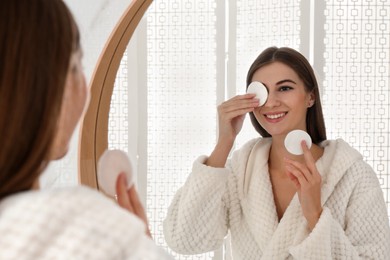 Young woman with cotton pads cleaning her face near mirror in bathroom