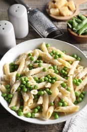 Delicious pasta with green peas, cheese and grater on wooden table