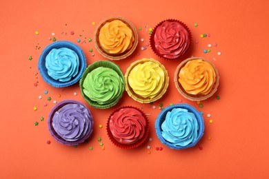 Photo of Delicious bright cupcakes and sprinkles on coral background, flat lay