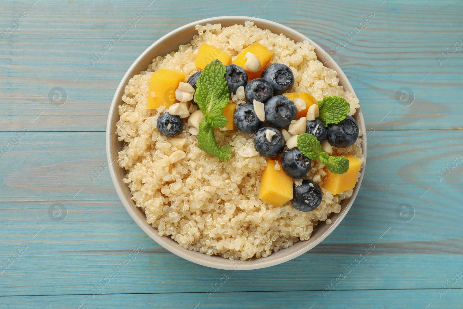 Photo of Tasty quinoa porridge with blueberries, pumpkin and mint in bowl on light blue wooden table, top view