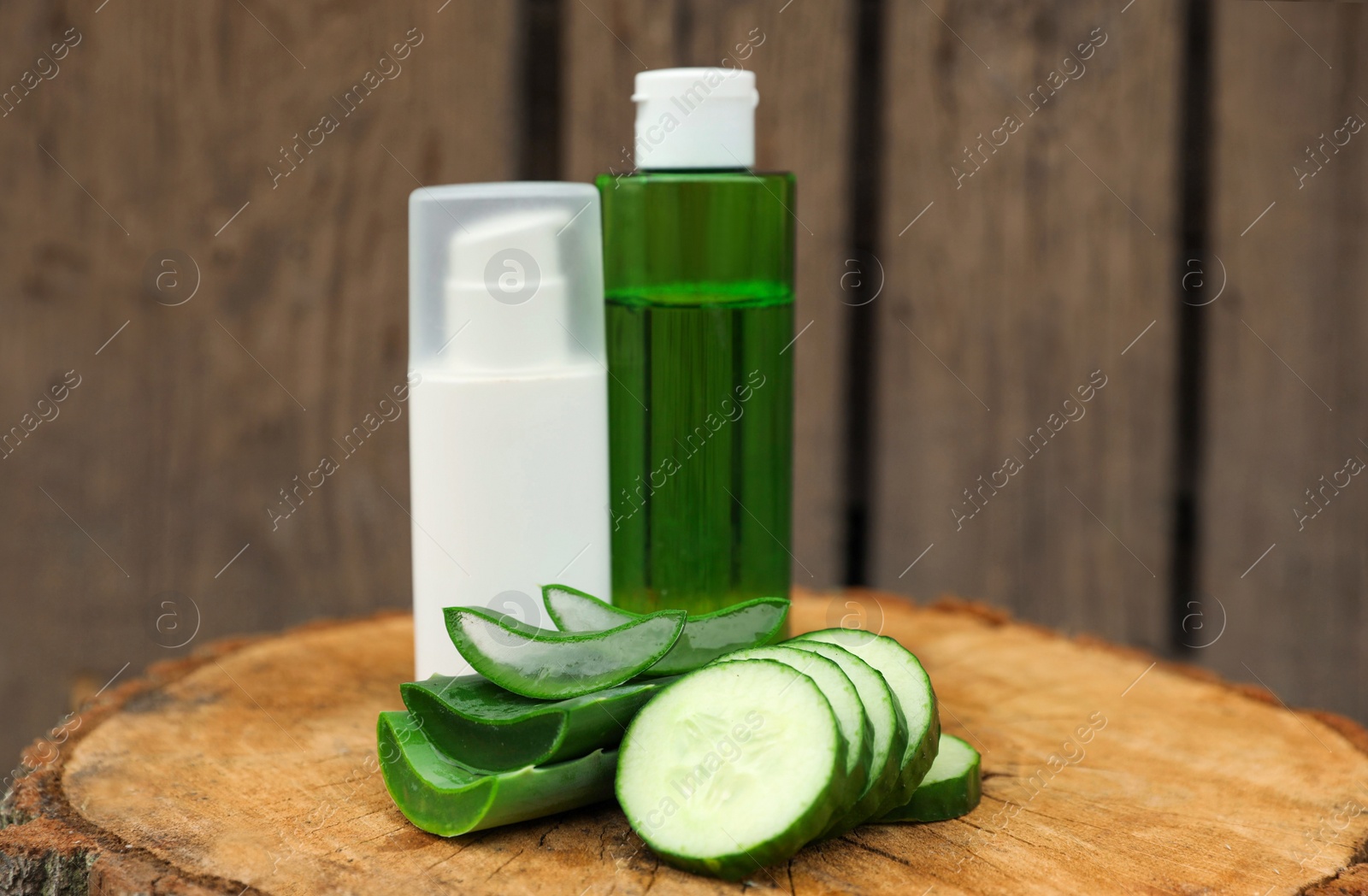 Photo of Bottles of cosmetic products, sliced aloe vera leaves and cucumber on wooden stump