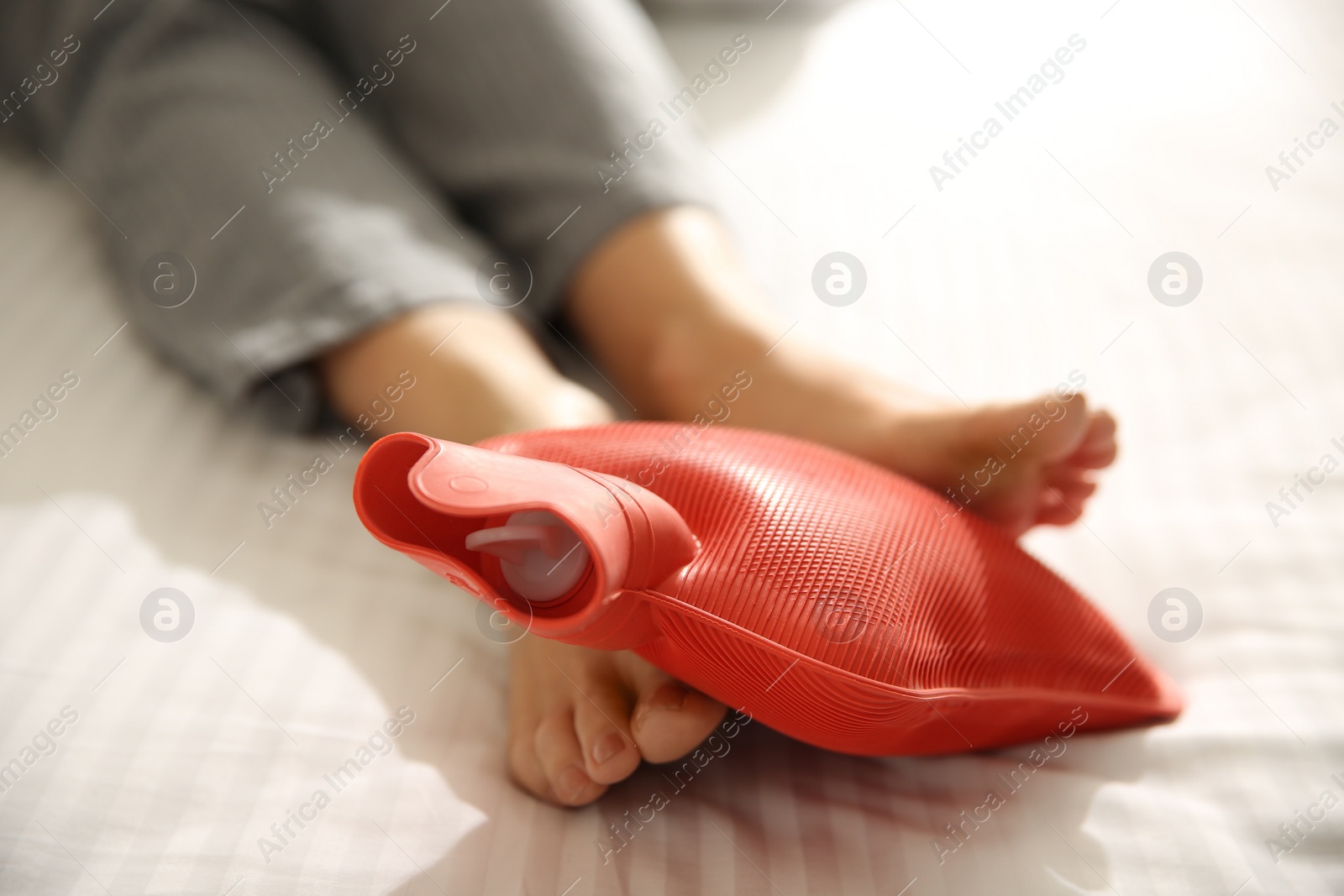 Photo of Woman warming feet with hot water bottle on bed, closeup