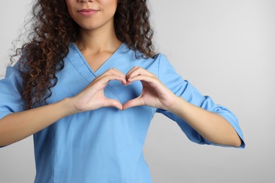 Photo of African-American doctor making heart with hands on light grey background, closeup