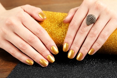 Photo of Woman showing manicured hands with golden nail polish on table, closeup