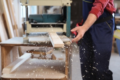 Photo of Working man using thickness planer at carpentry shop, closeup