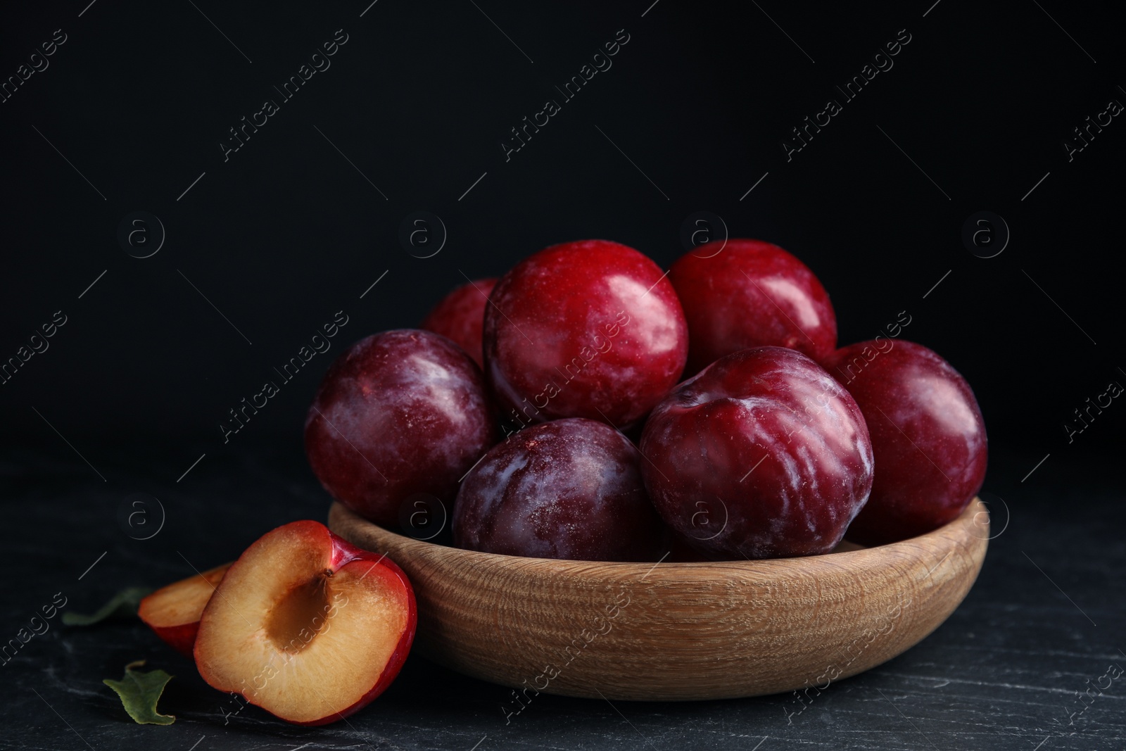 Photo of Delicious ripe plums in wooden bowl on black table