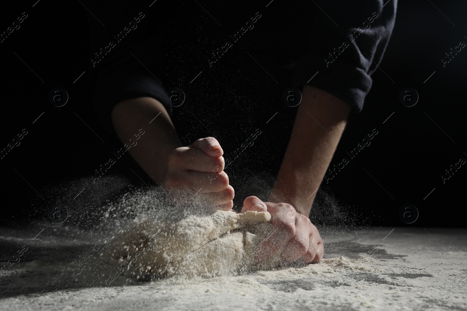 Photo of Making bread. Woman kneading dough at table on dark background, closeup