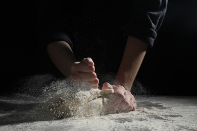 Making bread. Woman kneading dough at table on dark background, closeup