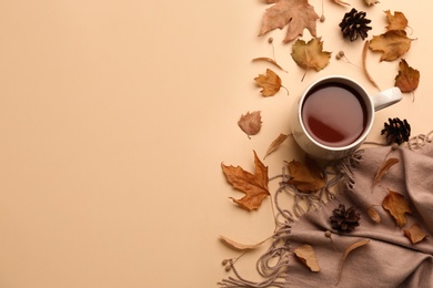 Flat lay composition with cup of hot drink, scarf and autumn leaves on beige background, space for text. Cozy atmosphere