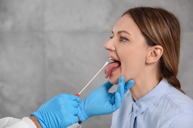 Photo of Doctor taking throat swab sample from woman`s oral cavity indoors. Space for text