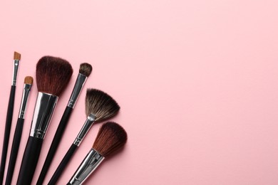 Different makeup brushes on pink background, flat lay. Space for text