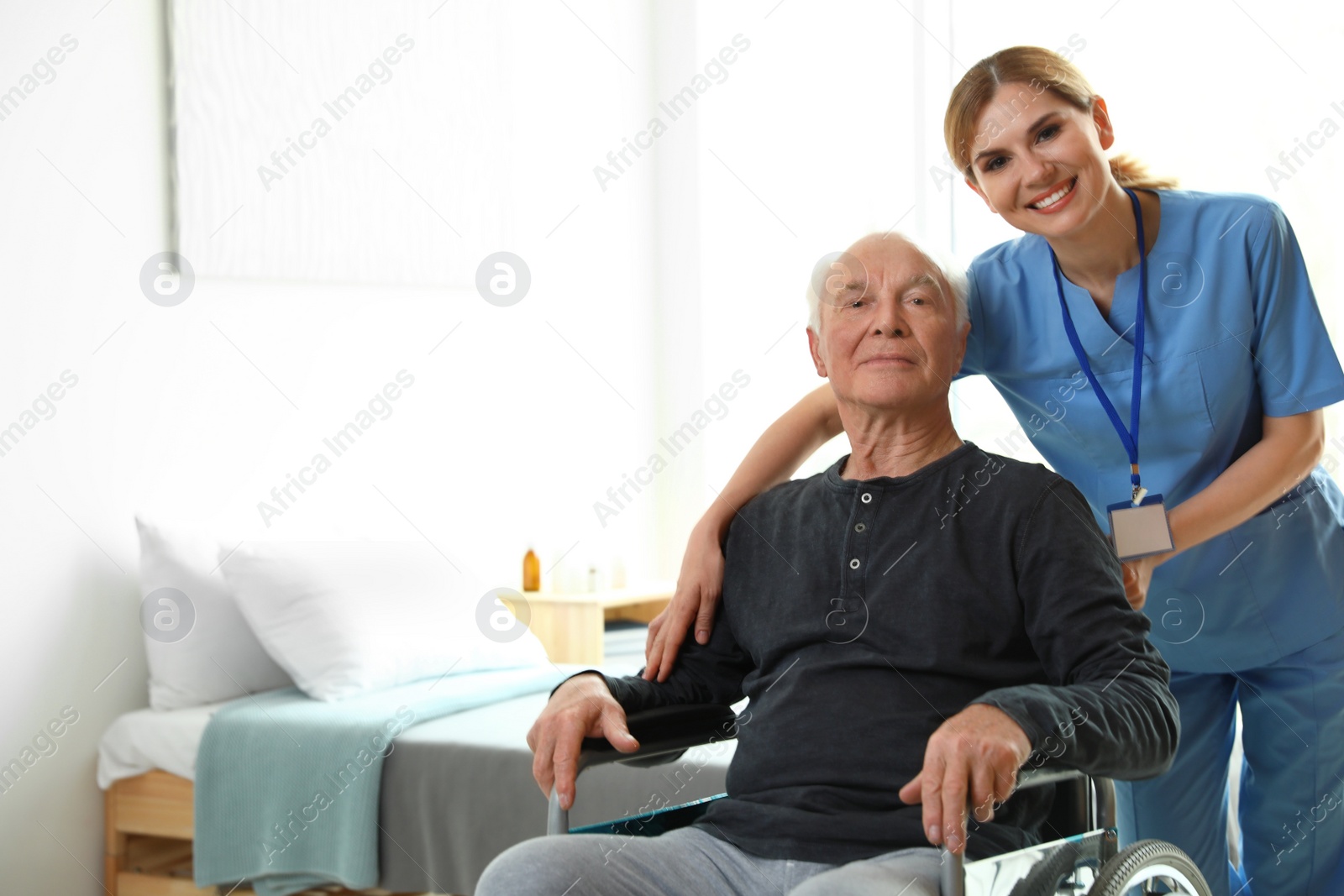 Photo of Nurse assisting elderly man in wheelchair indoors. Space for text