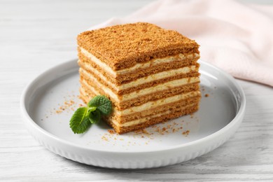 Photo of Slice of delicious layered honey cake with mint served on white wooden table