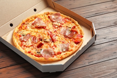 Carton box with delicious pizza on wooden background
