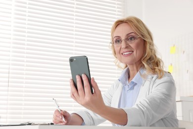 Photo of Doctor with glasses and smartphone consulting patient in clinic. Online medicine concept