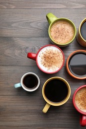 Many different cups with aromatic hot coffee on wooden table, flat lay