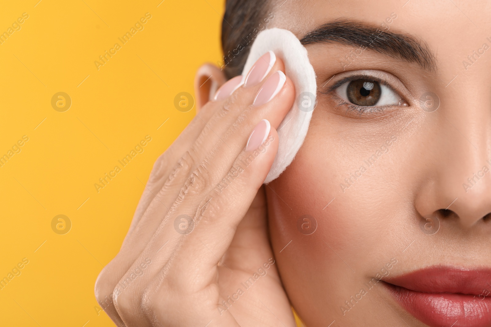 Photo of Beautiful woman removing makeup with cotton pad on orange background, closeup. Space for text