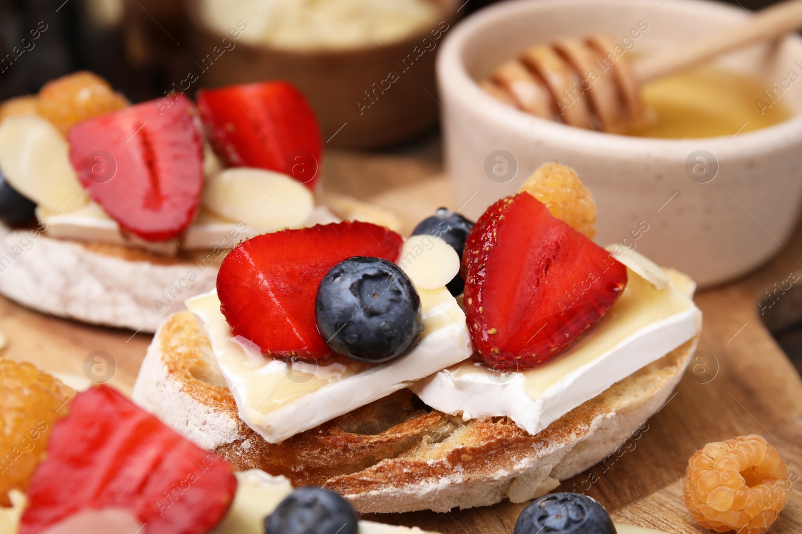 Photo of Tasty sandwiches with brie cheese, fresh berries and almond flakes on wooden board, closeup