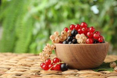 Different fresh ripe currants and green leaf on wicker surface outdoors, space for text