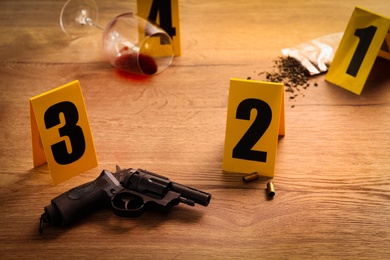 Photo of Crime scene markers, gun and shell casings on wooden table