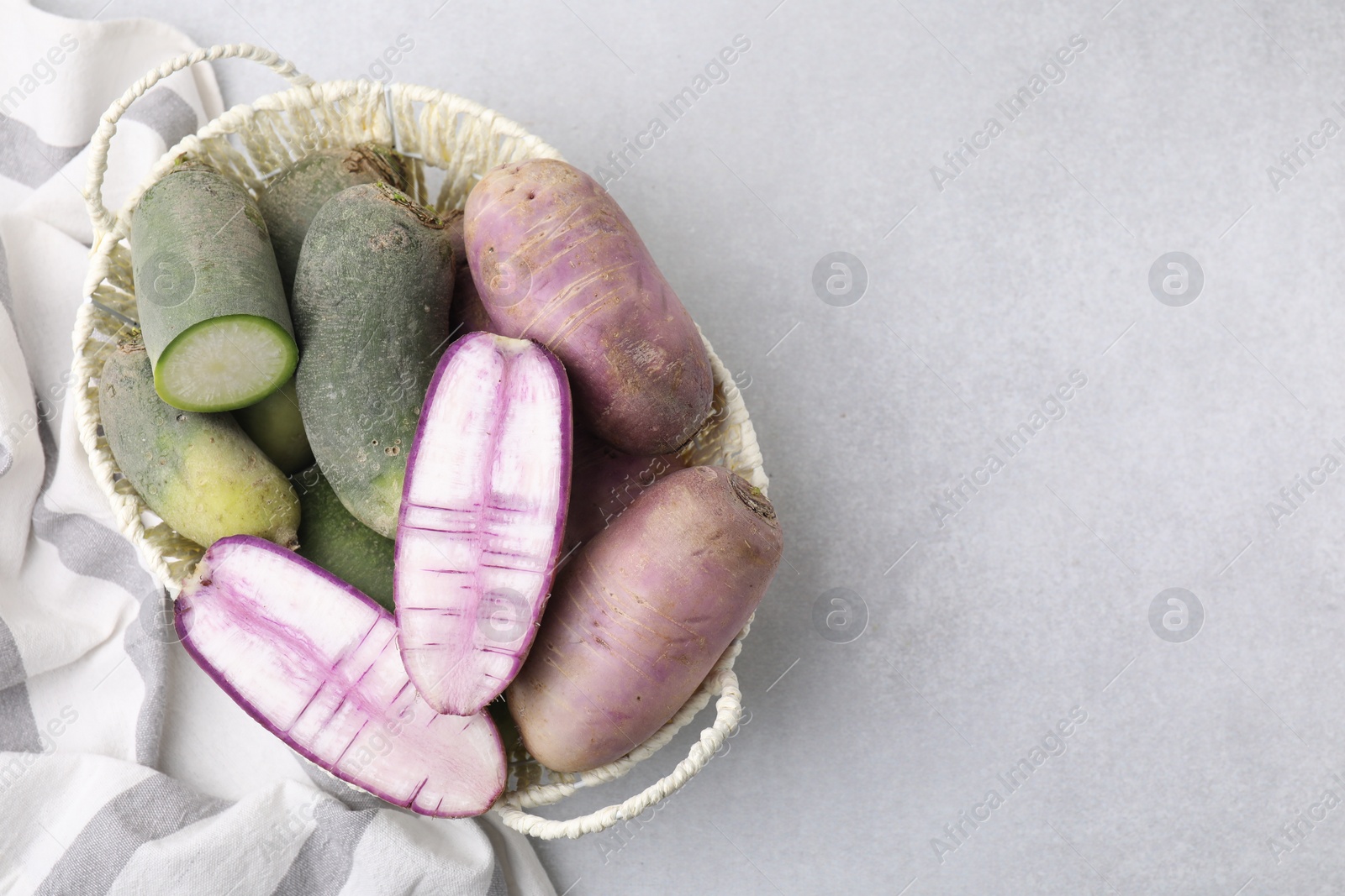 Photo of Purple and green daikon radishes in wicker basket on light grey table, top view. Space for text