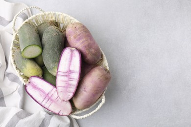Photo of Purple and green daikon radishes in wicker basket on light grey table, top view. Space for text