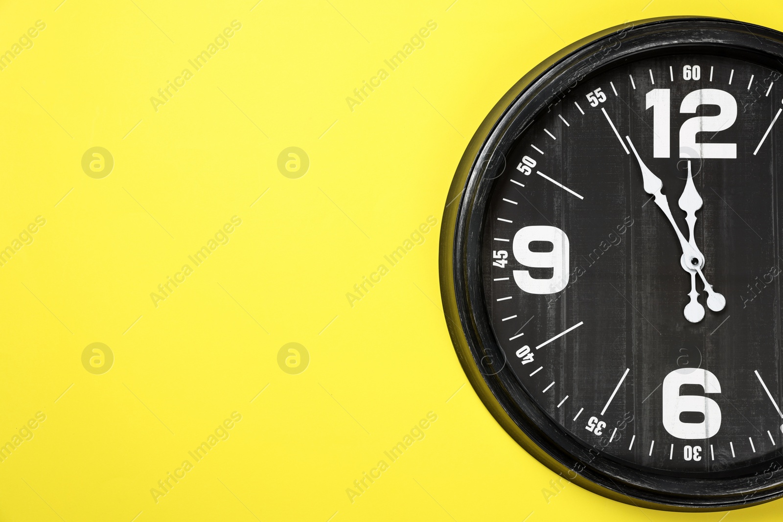 Photo of Clock showing five minutes until midnight on yellow background, space for text. New Year countdown