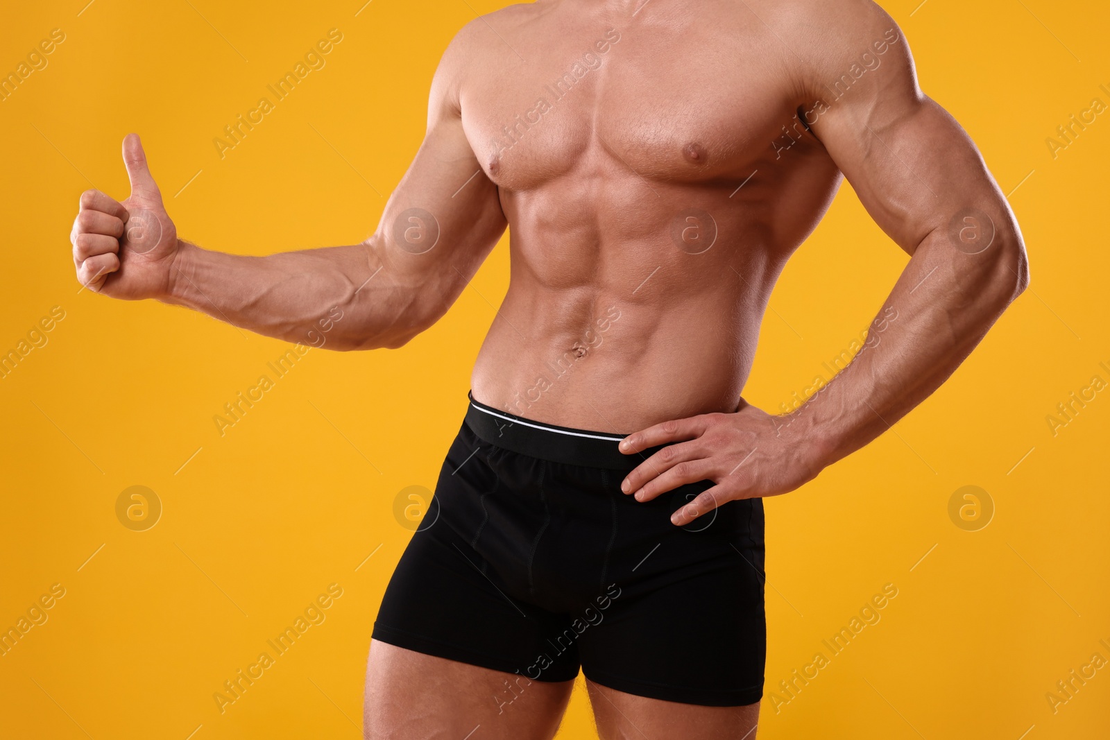 Photo of Young man is stylish black underwear showing thumb up on orange background, closeup