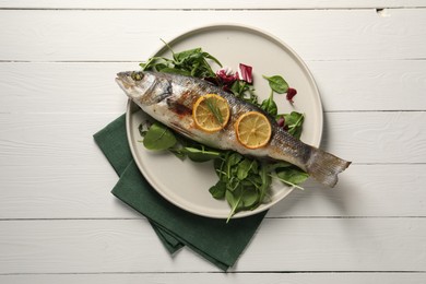 Baked fish with spinach and lemon on white wooden table, top view