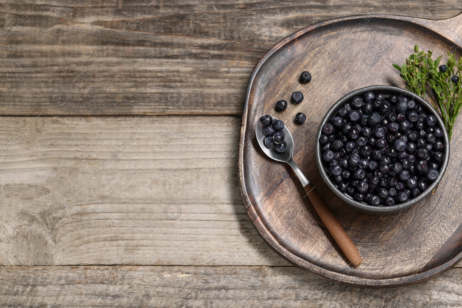 Photo of Ripe bilberries and sprigs with leaves on wooden table, top view. Space for text